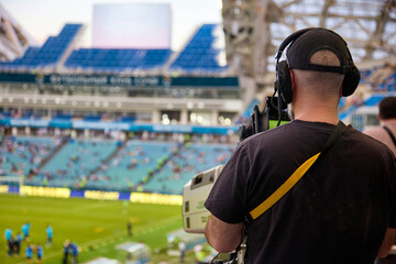 Rear view of an experienced video operator wearing headphones with a professional camera during a...