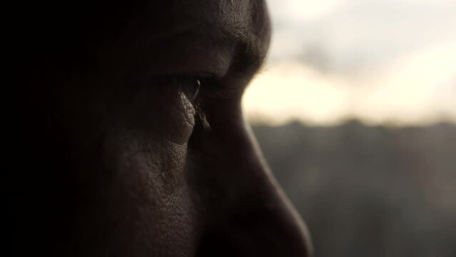 Dramatic isolated portrait of a man who opens his eyes and looks out the window with sad pensive look. Closeup of male eye. Slow motion. A man is worried and thinking while looking into the distance.