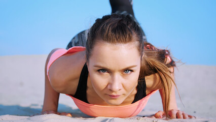 Healthy, young beautiful woman doing, performs push-ups,on the beach, at sunrise, Makes exercises for balance and coordination, deep muscle tone. Close-up, portrait