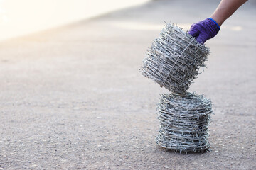 Closeup worker hand holds roll of barbed wire. Concept, construction tool. Barbed wire is used for make fences , secure property ,make border to show the territory of  area.       - Powered by Adobe
