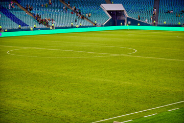High stands of the football stadium are gradually filled with fans and supporters. Large green field for playing football prepared before the match