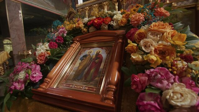 Russia, Republic of Dagestan - July 11, 2022: Icon with saints in a wooden frame and decorated with flowers on a lectern in the orthodox church