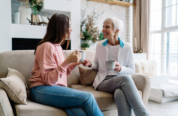 Senior multiracial women smiling while resting on sofa and talking