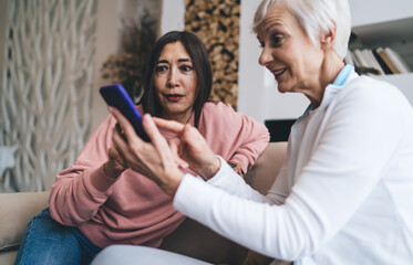 Amazed diverse girlfriends browsing cellphone together