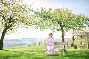 Outdoor portrait of happy pregnant woman enjoying nice sunny day in spring garden