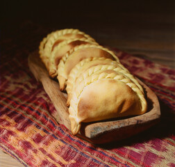 Empanadas, tanty, traditional Argentinian baked goods on a wooden plate and textile background
