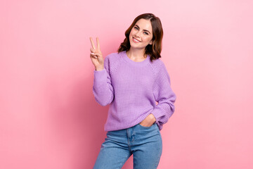 Photo of satisfied adorable woman with wavy hairstyle wear knit sweater showing v-sign arm in pocket isolated on pink color background