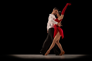 Passionate attractive young man and woman, professional ballroom dancers dancing tango over black background. Concept of hobby, lifestyle, action, beauty of movements, emotions, fashion, art - obrazy, fototapety, plakaty