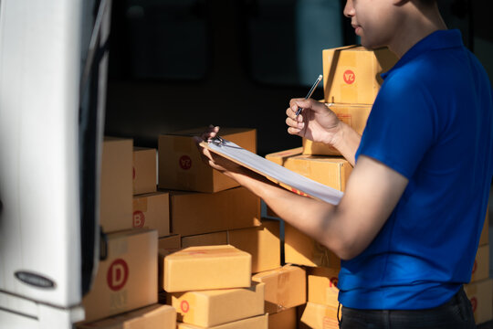 Professional delivery man checking delivery list before handed to his customer. standing next to his car with parcel boxes.