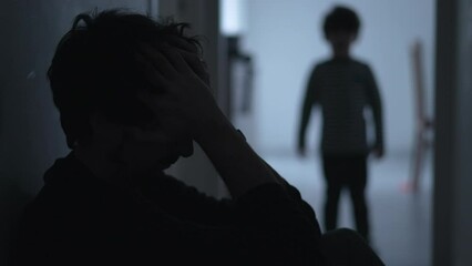 Dramatic scene of father suffering from financial difficulties while consolated by son. Small boy embracing dad during hard times. Parent suffering in the dark with kid