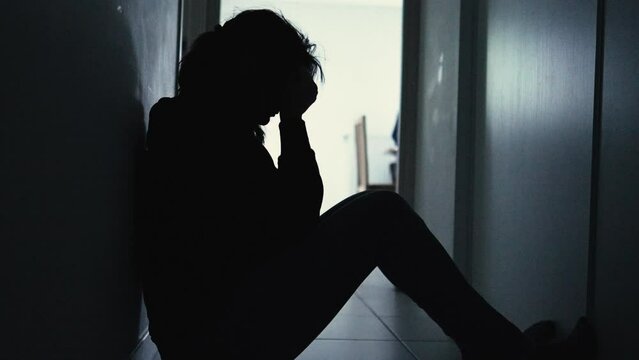 Silhouette of a frustrated woman sitting at home in the dark suffering from depression