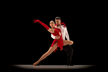 Passionate attractive young man and woman, professional ballroom dancers dancing tango over black background. Concept of hobby, lifestyle, action, beauty of movements, emotions, fashion, art - obrazy, fototapety, plakaty