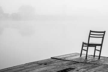 chair on the pier on the shore of the lake in foggy weather. Black and white image.