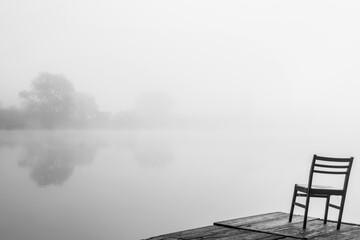 chair on the pier on the shore of the lake in foggy weather. Black and white image.