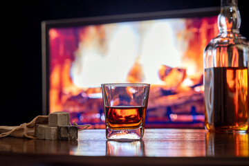 Whiskey in a glass with gray whiskey chilling stones on the background of a burning fireplace.