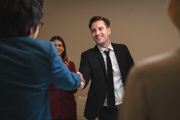 Senior, matured and successful business man in formal clothing greeting and welcoming and closing deal with young female partner and client in modern office by handshake