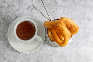Churros basket with cup of chocolate seen from above on gray stone background, typical Spanish breakfast