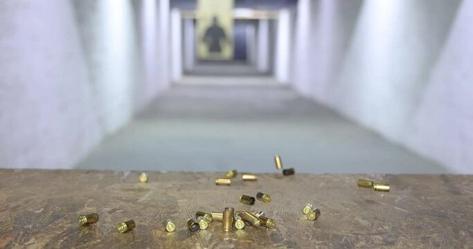 Empty bullet shells fall down after firing in indoor shooting range, slow motion. Gun shooting at a target, close up