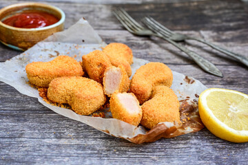 
 Crispy oven baked  chicken nuggets and ketchup. Breaded chicken fillets  with chilly peppers and fresh basi on wooden rustic background