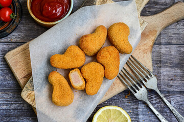 
 Crispy oven baked  chicken nuggets and ketchup. Breaded chicken fillets  with chilly peppers and fresh basi on wooden rustic background