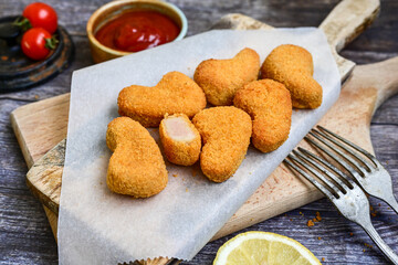 
 Crispy oven baked  chicken nuggets and ketchup. Breaded chicken fillets  with chilly peppers and fresh basi on wooden rustic background