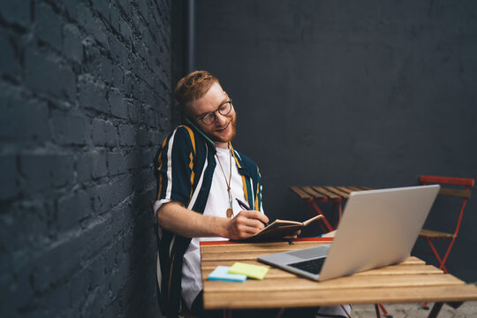 Happy freelancer taking notes while working in cafe and talking by phone