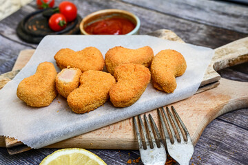 
 Crispy oven baked  chicken nuggets and ketchup. Breaded chicken fillets  with chilly peppers and fresh basi on wooden rustic background