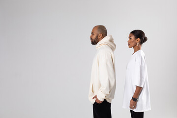 An african american man in a white hoodie and a woman in a white t-shirt stand on a white background.