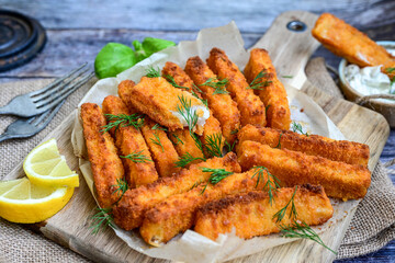 Close up of   Crispy breaded  deep fried fish fingers with breadcrumbs served  with remoulade sauce and  lemon Cod Fish Nuggets on rustic wood table background