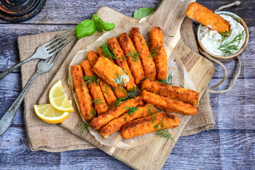 Close up of   Crispy breaded  deep fried fish fingers with breadcrumbs served  with remoulade sauce and  lemon Cod Fish Nuggets on rustic wood table background