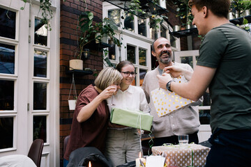 Side view of man giving gift to sister while standing at restaurant