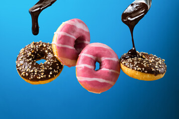 Front view of flying donuts with two spoons pouring dark chocolate on them