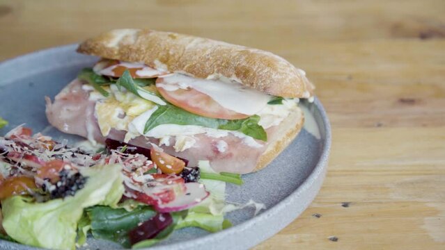 Plano a detalle de emparedado de jam&oacute;n acompa&ntilde;ado de ensalada, queso, aderezo, vegetales sobre mesa