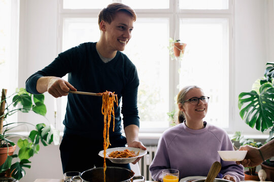 Smiling man removing spaghetti in plate at home