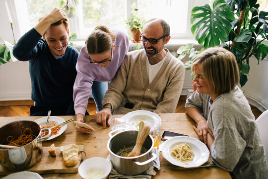 Girl Sharing Smart Phone With Family At Dining Table