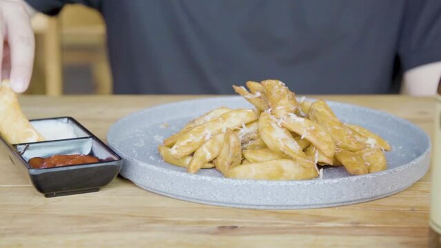 Plano a detalle de Plato de papas gajo con queso sobre una mesa de madera untando aderezo.