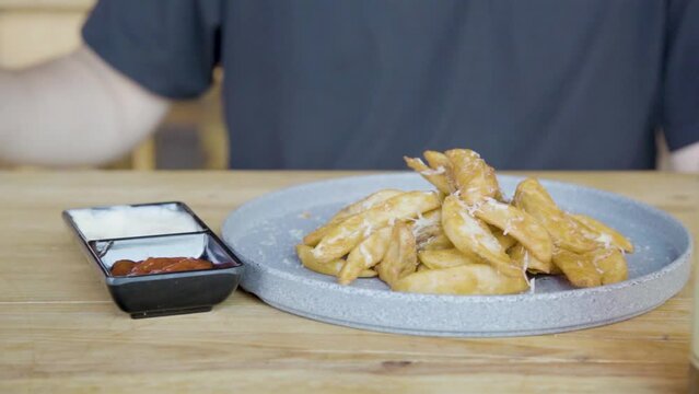 Plano a detalle de Plato de papas gajo con queso sobre una mesa de madera untando aderezo.