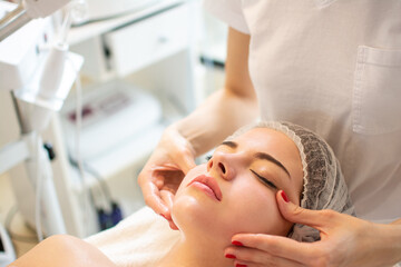 Obraz na płótnie Canvas Close up of beautiful young woman having curative facial cheeks massage in beauty salon.
