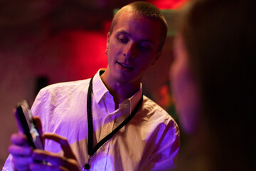 Young businessman sharing mobile phone with colleague in illuminated workshop