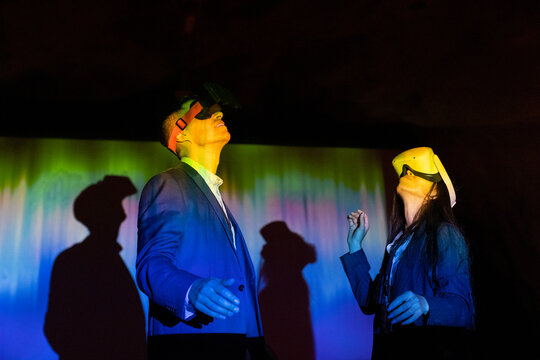 Female and male colleagues watching through virtual reality glasses in illuminated exhibition center
