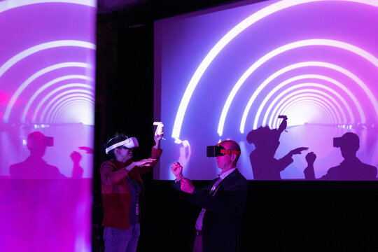 Colleagues with virtual reality glasses gesturing by projection screen at exhibition center