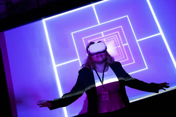Young female entrepreneur wearing virtual reality glasses in front of projection screen at workshop