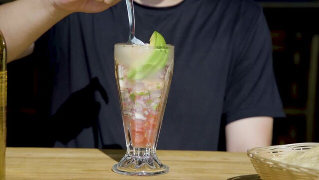 Persona batiendo un coctel de camar&oacute;n y pulpo sobre una mesa del atardecer en un restaurante.