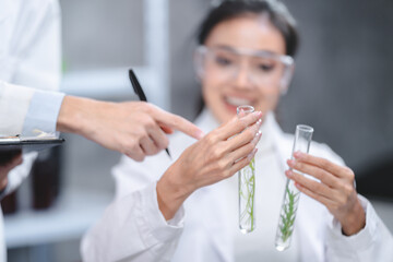 Obraz na płótnie Canvas Young Asian male and female scientist partners wearing lab coat with protective eye wear and glasses practicing research on plant while taking notes on a notepad in modern laboratory