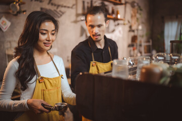 Smiling young female barista with male colleague in apron preparing coffee while holding filter and equipment while preparing beverage for customer in modern cafe