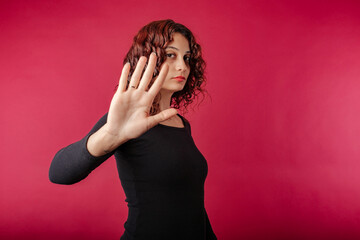 Portrait of cute redhead woman wearing black ribbed dress standing isolated over red background...