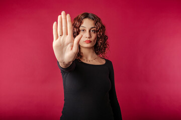 Redhead millennial woman wearing black dress standing isolated over red background doing stop sing...