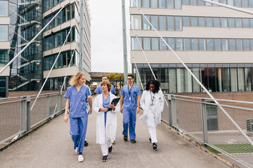 Multiracial healthcare workers discussing while walking on bridge by hospital building