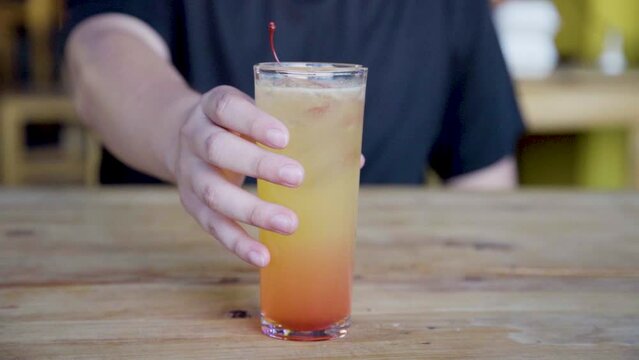 Colorida bebida de tequila con jugo de naranja, sangr&iacute;a y cereza, sobre una mesa de madera	