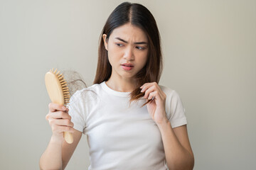 Serious asian young woman holding brush holding comb, hairbrush with fall black hair from scalp after brushing, looking on hand worry about balding. Health care, beauty treatment, hair loss problem.